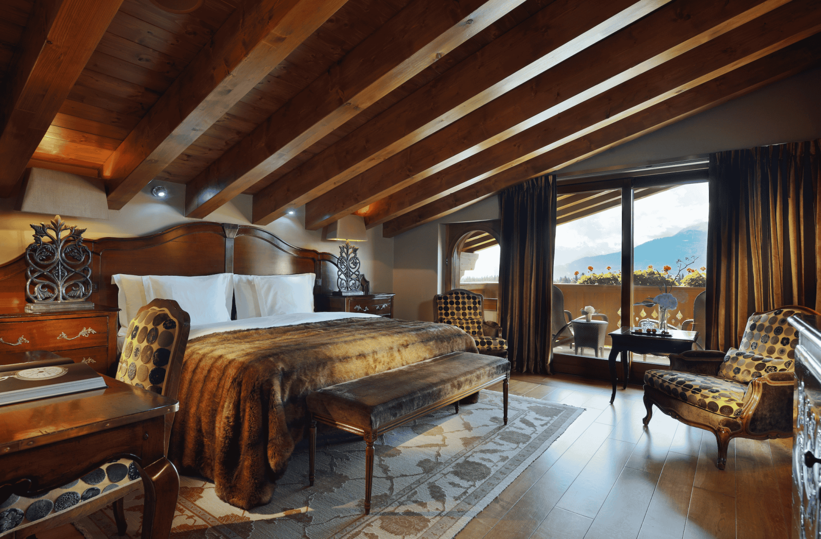 Elegant alpine suite at Guarda Golf Hotel & Residences featuring wooden beams, mountain views, and cozy luxury decor.